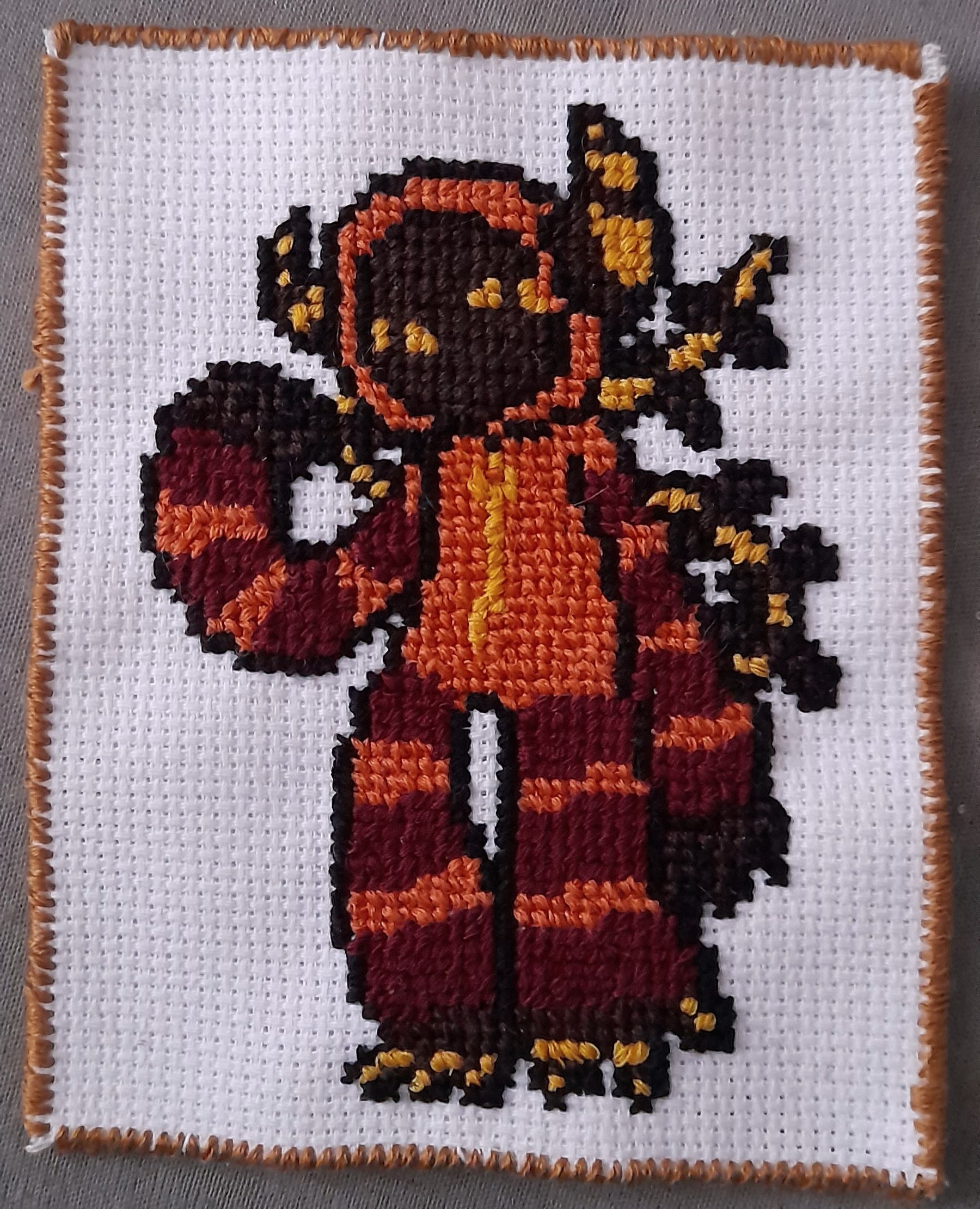 a cross-stitch of clyde, a demon with a long spiked tail and horns wearing a striped orange and maroon zip up onesie