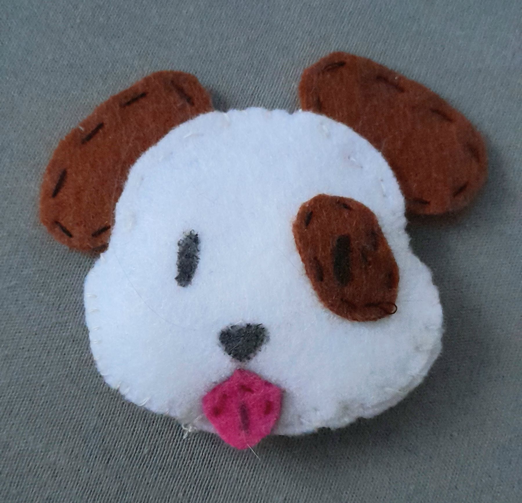 small plushie of a dog head emoji. the dog is white with brown ears and patch on one of its eyes