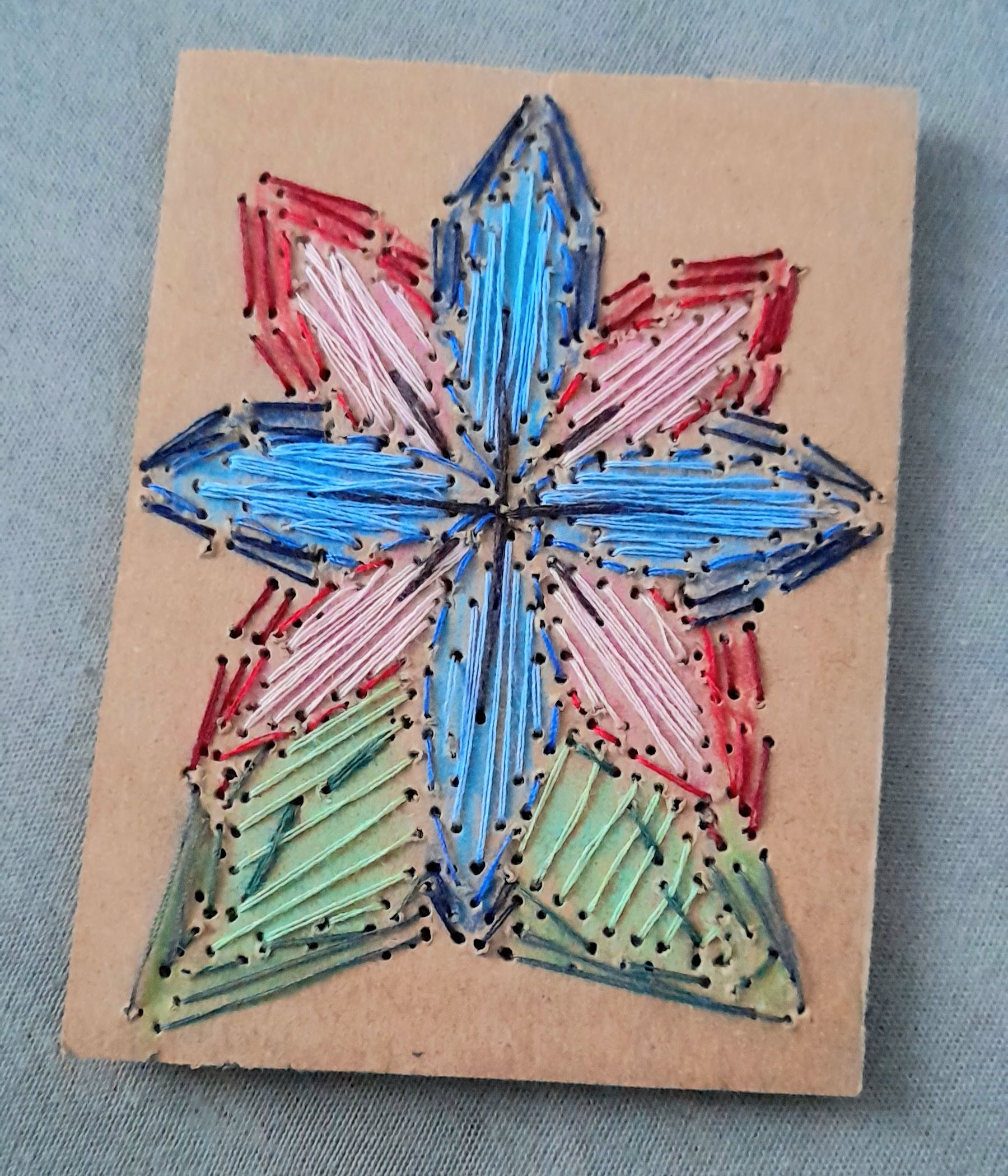 a red and blue flower embroidered on a piece of cardboard